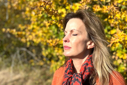 Smiling mature woman wearing a scarf in autumn woodland, representing winter skin care tips and non-invasive facial treatments in Essex, Hertfordshire and Cambridgeshire
