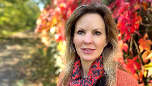 Smiling woman outdoors surrounded by autumn leaves, representing radiant skin and confidence during menopause – Sculpted Skincare, Heydon